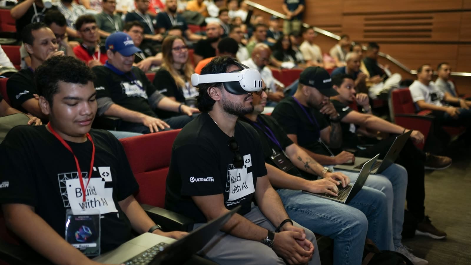 Un participante con gafas de realidad virtual mientras sus compañeros trabajan en portátiles