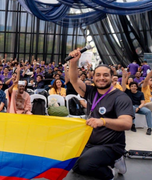 Anuar Harb, cofundador, sostiene un micrófono y una bandera de Colombia frente al público de un evento