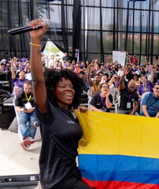 Grace Torres, cofundadora, sostiene un micrófono y una bandera de Colombia frente al público de un evento